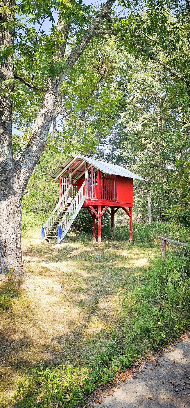 The Club House, a red elevated playhouse with a white staircase under the trees