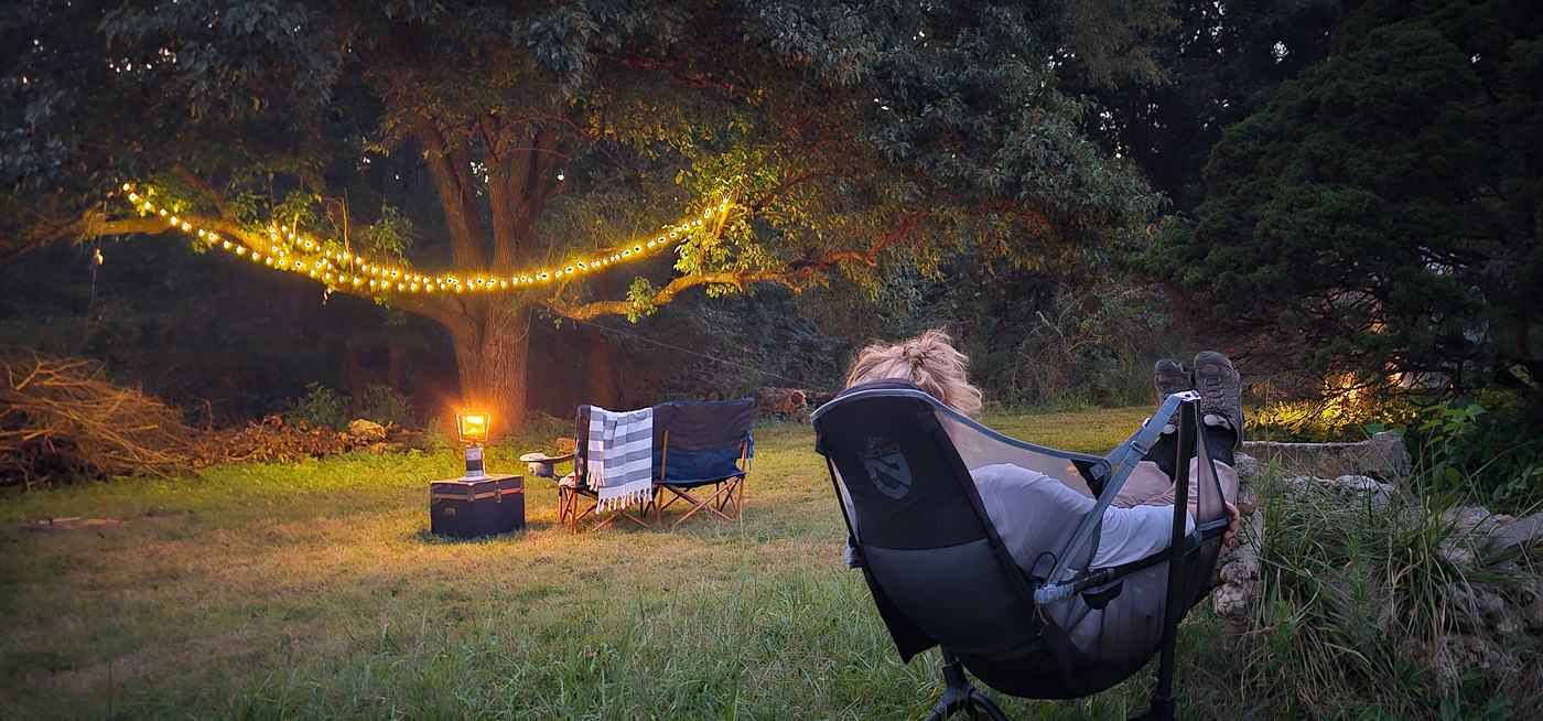 Someone reclined in a camp chair with their feet up under string lights