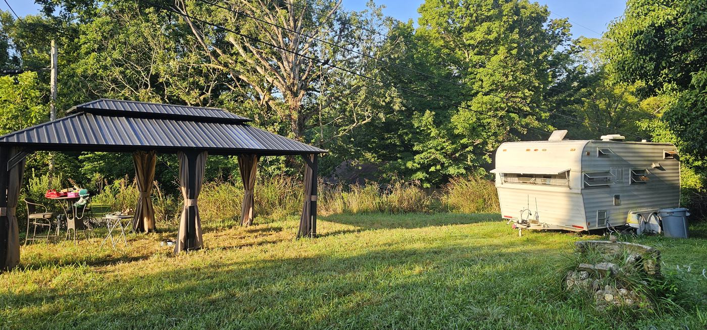 The gazebo with curtains and a table beside the white vintage camper in morning sun